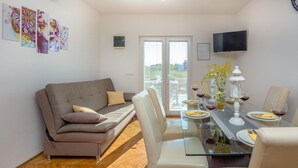 En moderne stue med sofa, spisebord dækket til to personer og et fjernsyn hængt på væggen.