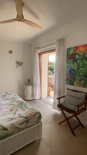 Une chambre à coucher comprenant un lit, une chaise, un ventilateur de plafond, un radiateur, un tableau et une vue sur l’extérieur.