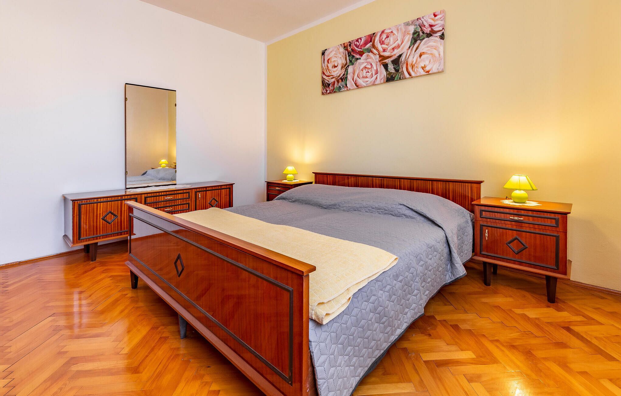 A bedroom with a wooden bed, two bedside tables, a mirror, and a floral artwork on the wall.