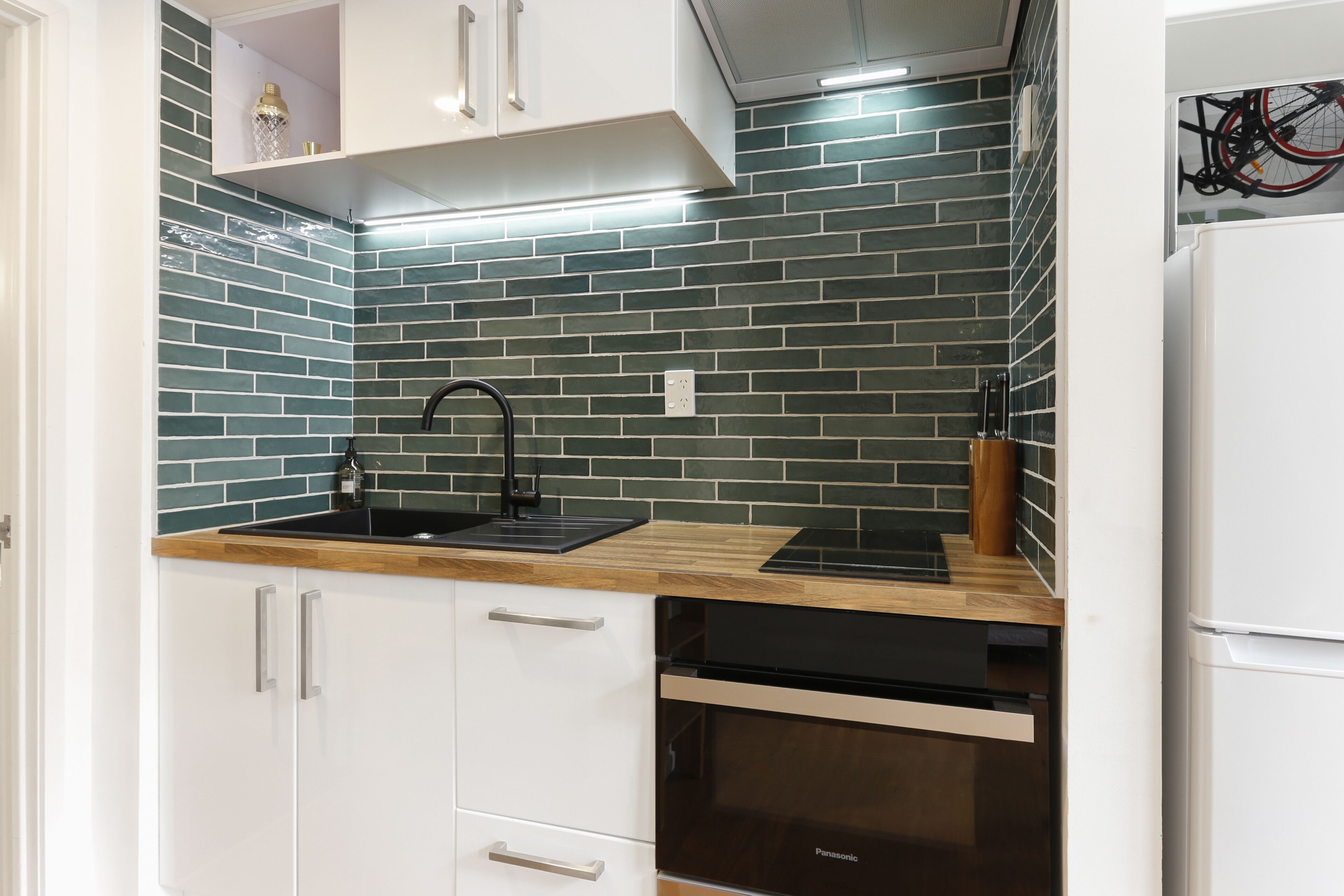 A kitchen with white cabinets, a black sink, and a Panasonic oven.