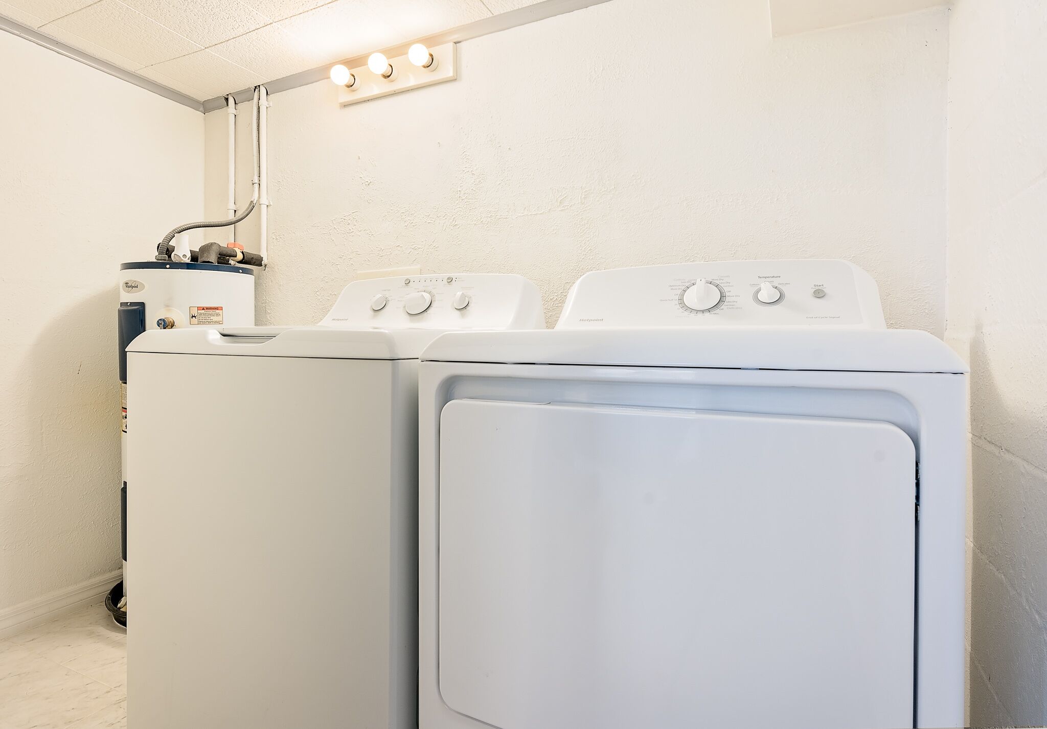 A laundry room with two stacked washers and dryers, a water heater, and a light fixture above.