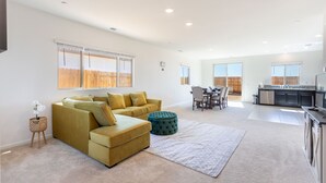 Un vaste espace de vie comprenant un canapé, un pouf et une table à manger avec des chaises.