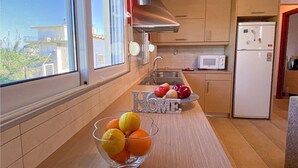 Una cocina moderna con una campana extractora de acero inoxidable, un microondas y un refrigerador. Hay un frutero sobre la encimera y una ventana que ofrece vistas al exterior.
