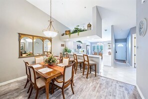 A dining area with a wooden table and chairs, a large mirror, and a hanging light fixture.