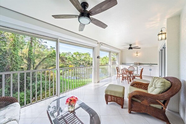 A spacious balcony with a view of a lush garden, wicker furniture, and ceiling fans.