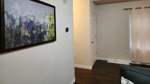 A living room with a large abstract painting, a door, and a window with curtains. - Beautiful Three Bedroom House (Kitchener)