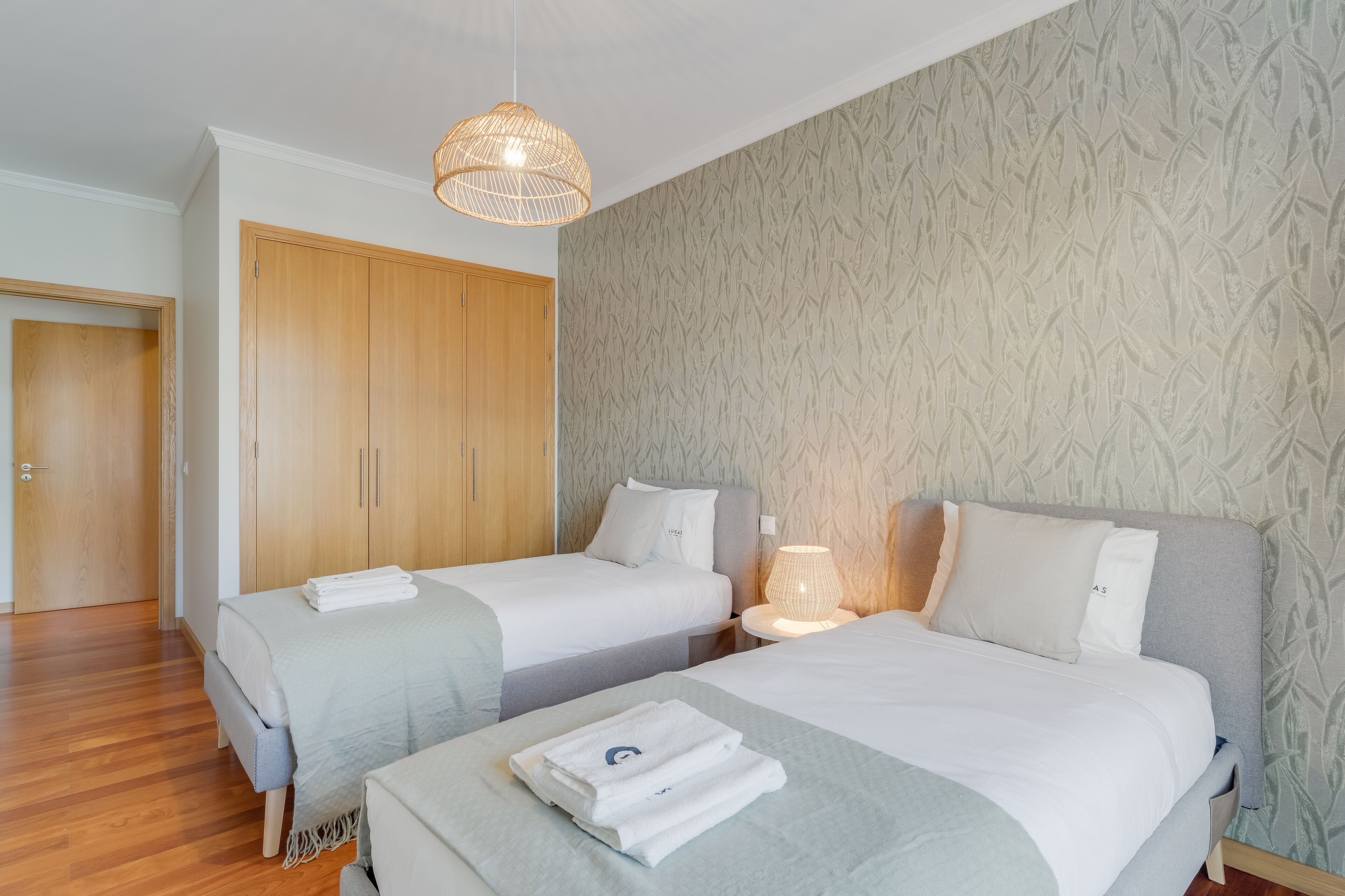 A hotel room with two beds, a wardrobe, and a patterned wallpaper.