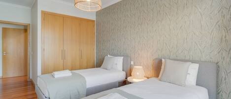 A hotel room with two beds, a wardrobe, and a patterned wallpaper.