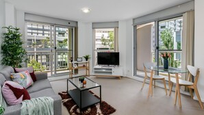 Una sala de estar moderna con sofá, televisor, mesa de centro de vidrio y comedor.
