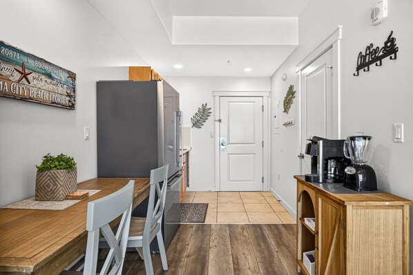 Cocina compacta con comedor, refrigerador, cafetera y un cartel decorativo en la pared.