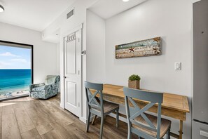 Ein Zimmer mit einem Holztisch, zwei Stühlen, einer Bank, einem an der Wand befestigten dekorativen Schild und Meerblick durch eine Tür.