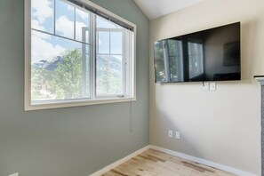 A room with a large window, a mounted flat-screen TV, and a light-colored wall. - Summit Place 4B | Great Value for a Family of 4 (Canmore)