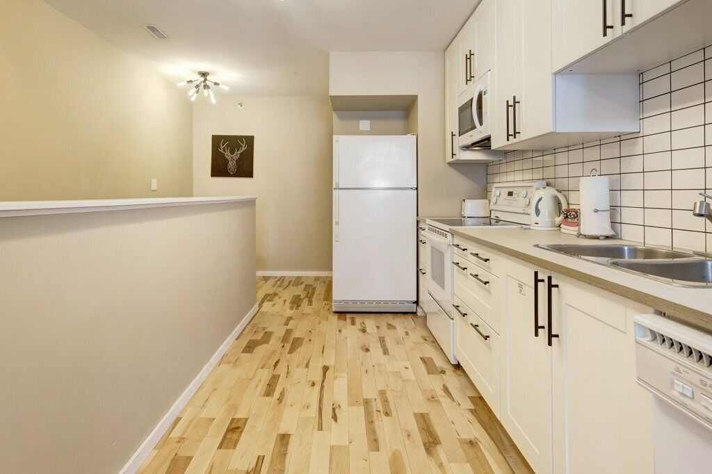 A compact kitchen with white cabinets, a refrigerator, a microwave, a kettle, and a dishwasher.
