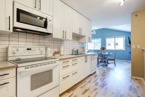A modern kitchen with white cabinets, a microwave, an oven, and a dining area with a table and chairs. - Summit Place 4B | Great Value for a Family of 4 (Canmore)