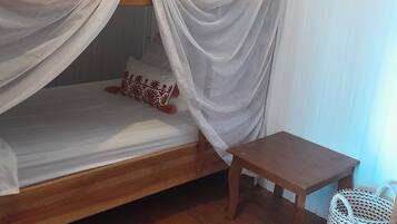 Un letto singolo con baldacchino, un tavolino di legno e un cesto fissato alla parete.