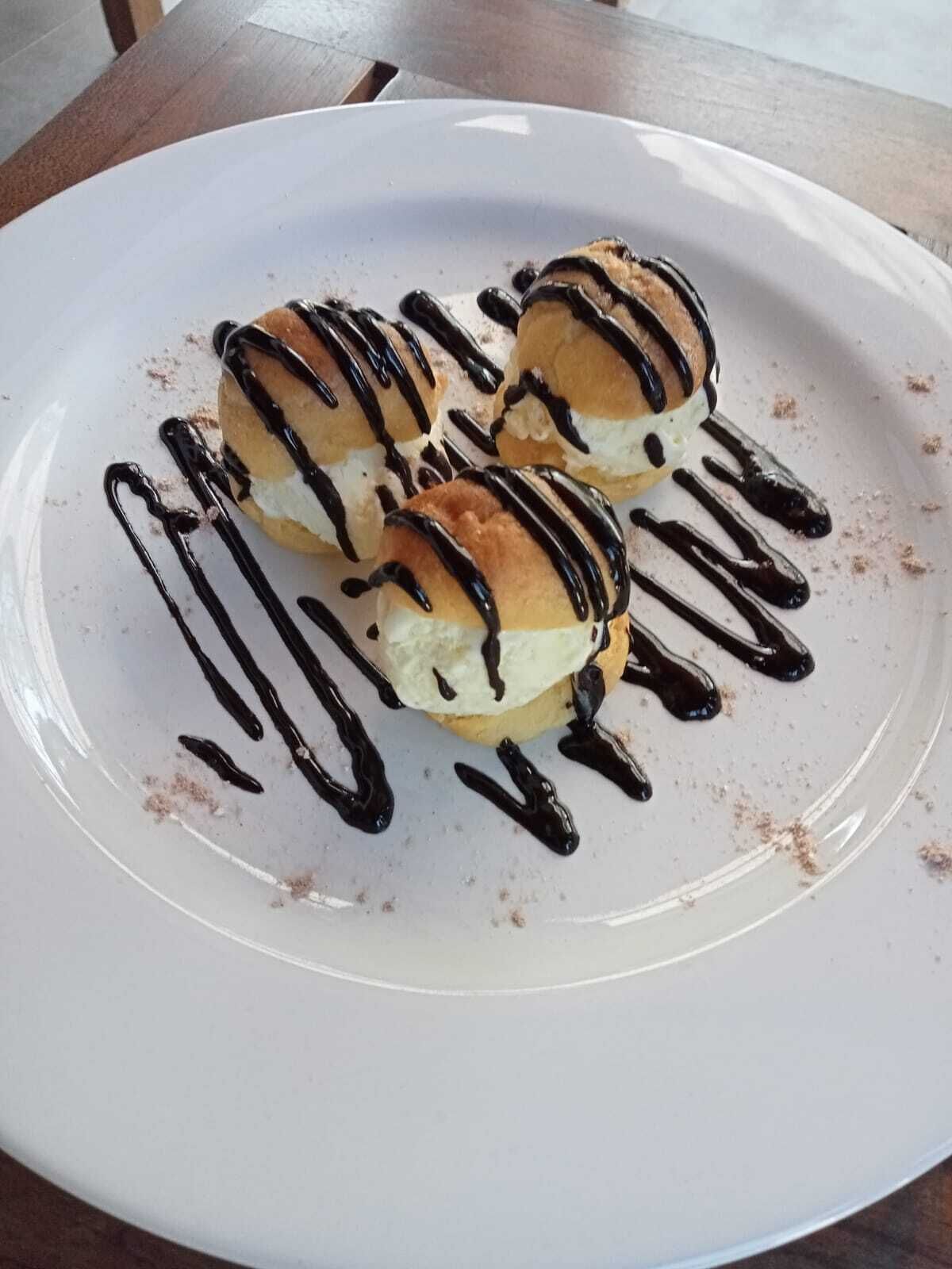 A plate with three éclairs drizzled with chocolate sauce.