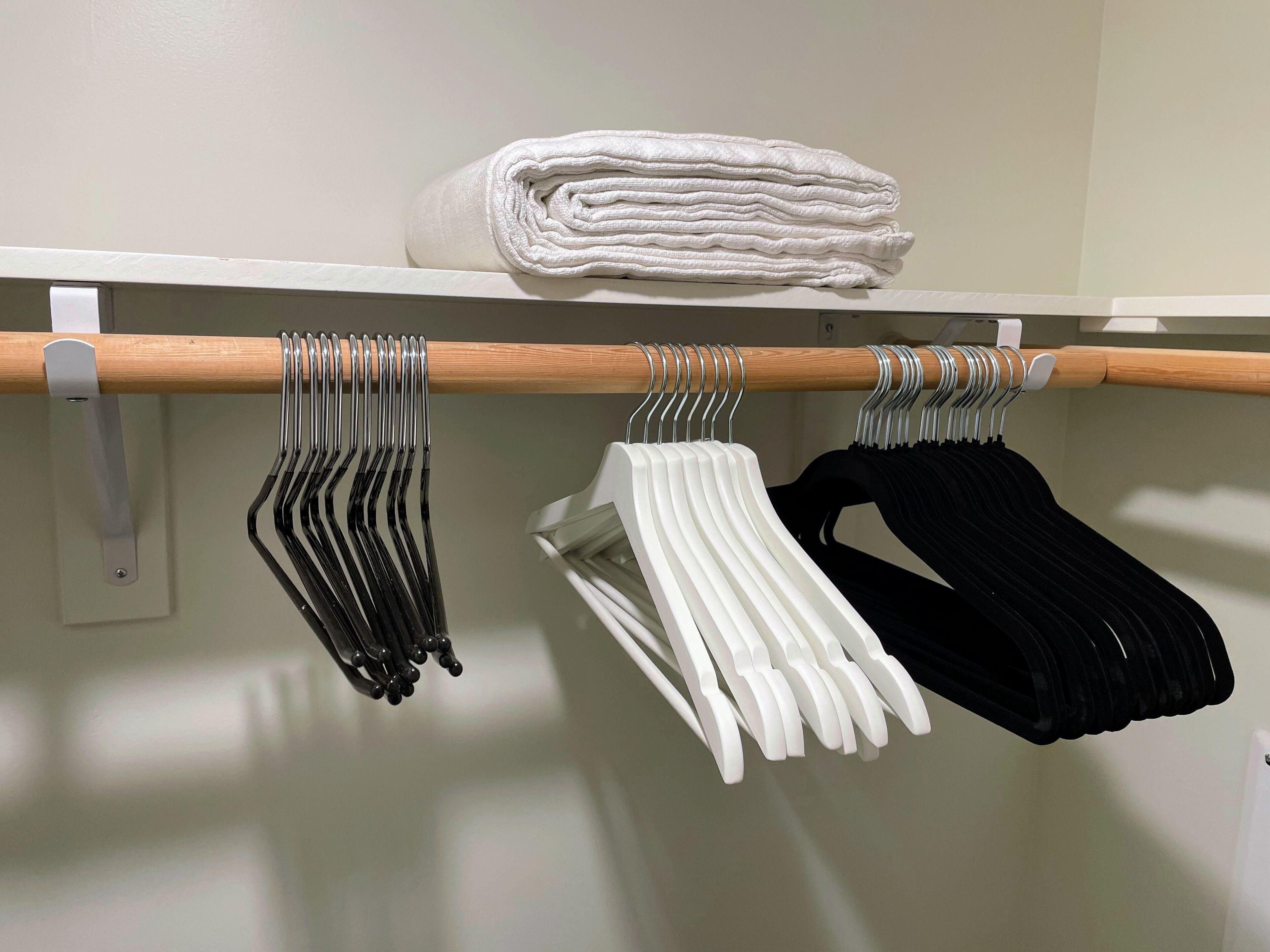 A closet with a wooden rod holding folded towels and a stack of folded towels on a shelf.