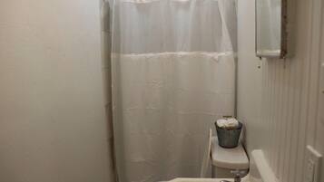 A small bathroom with a white shower curtain, a white sink, and a bucket on the wall.