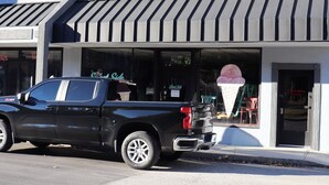 A black pickup truck parked in front of a building with a striped awning and a large ice cream cone decoration.