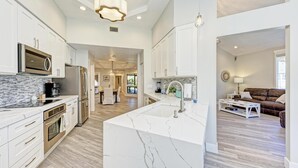 A modern kitchen with white cabinetry, a marble island, stainless steel appliances, and a central island sink.