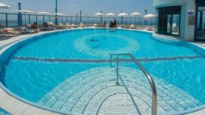 A swimming pool with a clear blue water, a lifeguard stand, and lounge chairs with umbrellas. - Beachside 2BR Apt with Sea & Skyline Views (Tel Aviv-Yafo)