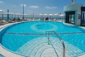 Una piscina con acqua cristallina, una postazione di salvataggio e lettini con ombrelloni.