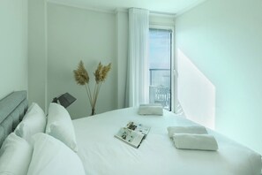 A hotel room with a neatly made bed, a window with curtains, and a view of the outside.