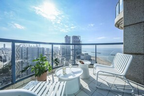 Un balcon avec vue sur la ville, une table avec une bouteille et un verre, et deux chaises blanches.