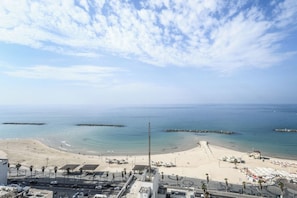 A beach with a clear sky, a road with vehicles, and a few buildings in the foreground.