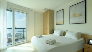 A hotel room with a large bed, a sliding glass door leading to a balcony, and two framed artworks on the wall. - Beachside 2BR Apt with Sea & Skyline Views (Tel Aviv-Yafo)