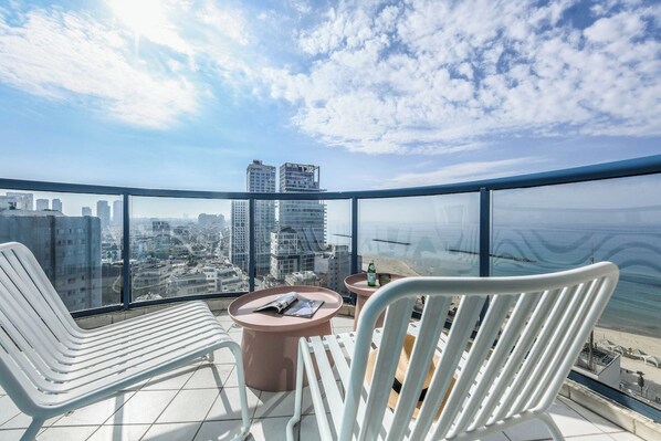 A high-rise balcony with a city view, two white chairs, a round table, and a bottle of water.