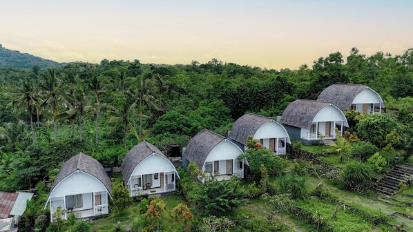 A row of dome-shaped cottages nestled in a lush, green landscape with a backdrop of hills. - The Kleep Jungle Resort (Penida Island)