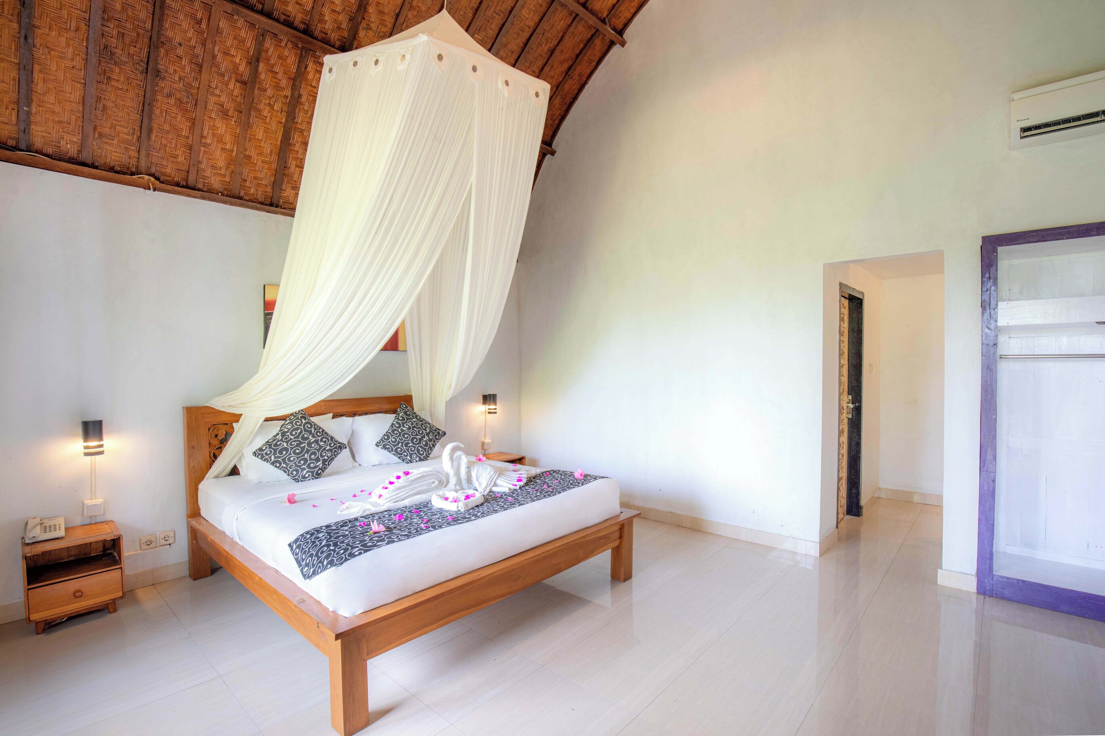 A bedroom with a wooden bed, white bedding, a canopy, bedside lamps, and a nightstand.