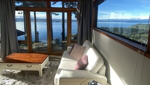 Een moderne woonkamer met een witte bank, een houten salontafel en uitzicht op een meer door grote glazen deuren.