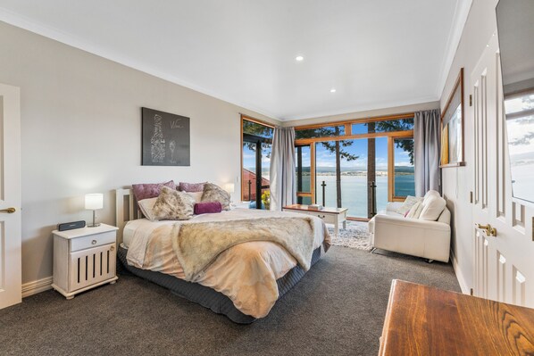 A bedroom with a large bed, a bedside table, a chair, and a view of the outdoors.