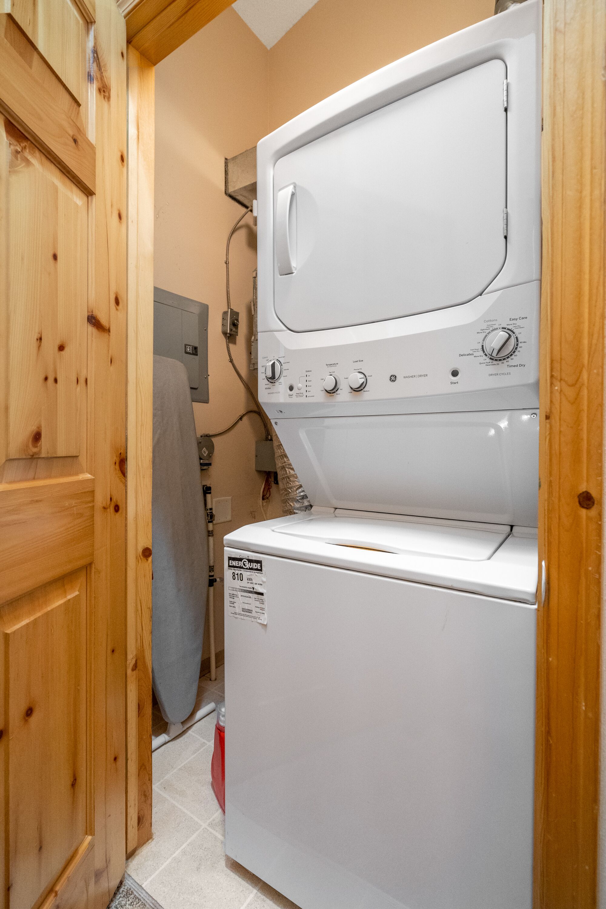 Ein Waschraum mit gestapelten Waschmaschine und Trockner, Holzausbau und einem sichtbaren Stromverteiler.