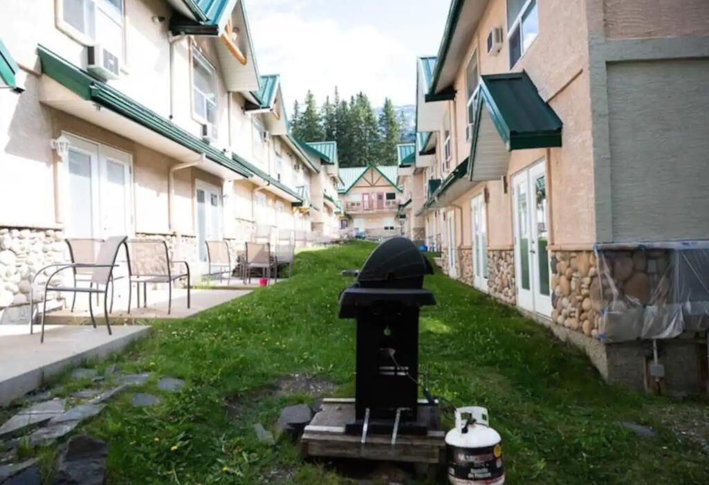 Een smal pad tussen gebouwen, met een barbecue en een propaantank op de voorgrond.