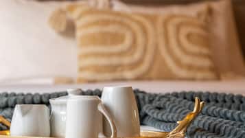 Un vassoio per la colazione ordinato, con una brocca, due tazze e un teiera, su un letto con un cuscino a righe e una coperta lavorata a maglia.