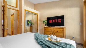 Habitación de hotel con una cama, un televisor mostrando 'NETFLIX', un aparador de madera y una pequeña planta.