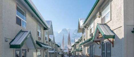 A snow-covered street with buildings on either side, featuring a central view of snow-capped mountains in the background.