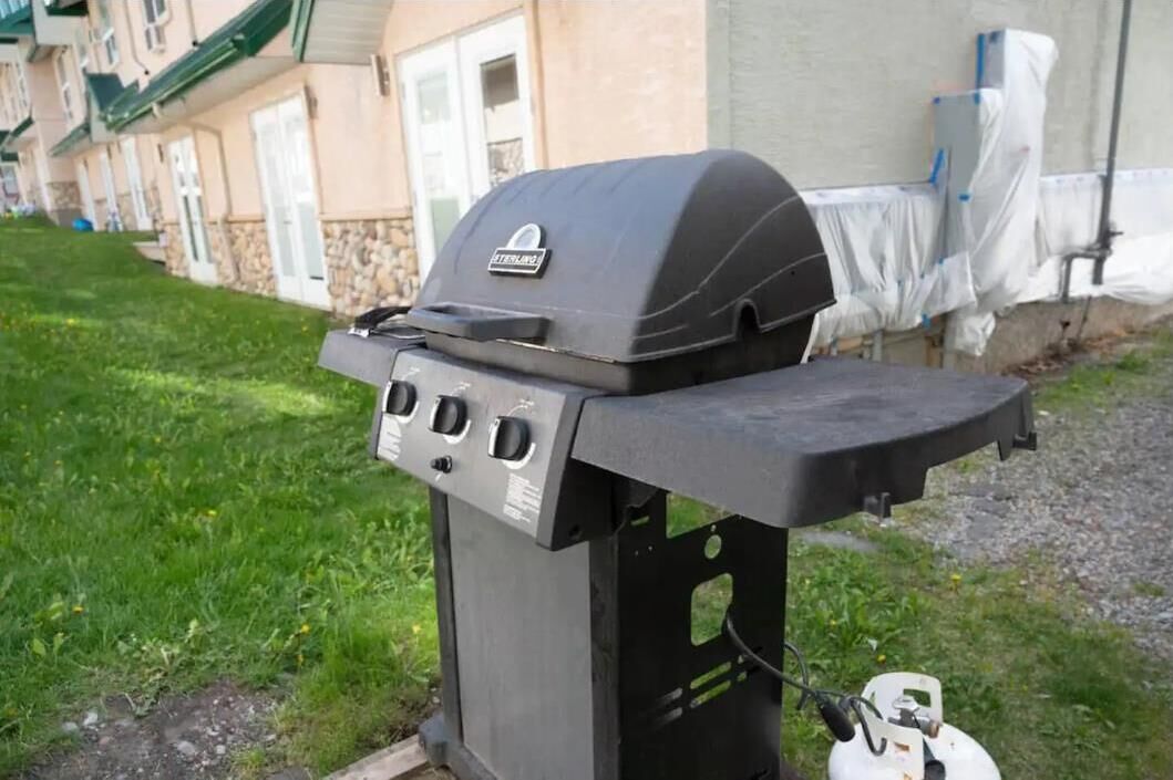 A portable gas grill with a control panel, set up outdoors in front of a building with a stone facade and a covered porch.