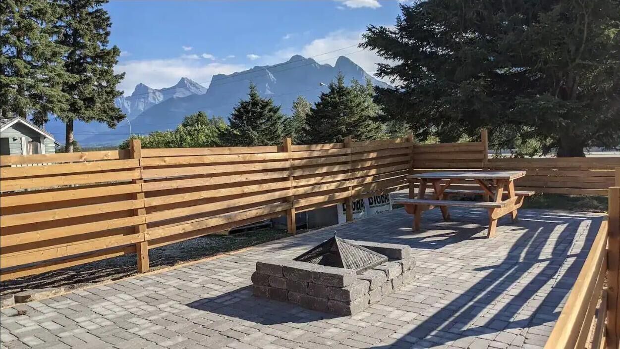 A wooden deck with picnic tables and a fire pit, surrounded by trees and mountains in the background.