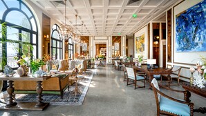 A spacious hotel lobby with a high ceiling, large windows, and a variety of seating arrangements including sofas and chairs.