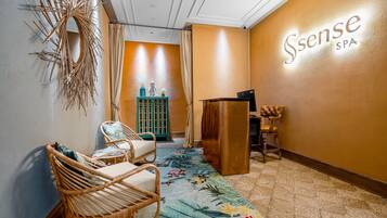 Un cuarto de spa con sillas de mimbre, alfombra floral, un atril de madera y un cartel en la pared que dice "Ssense SPA".