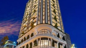 A tall, modern hotel with a curved facade, multiple balconies, and a well-lit entrance.