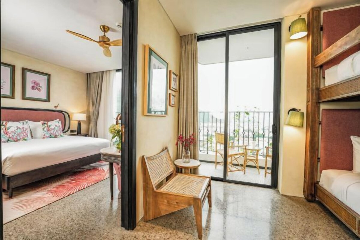 A hotel room with a bed, a chair, a balcony with a table, and a view of the outdoors.