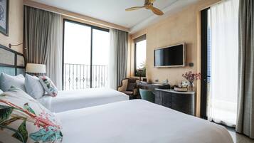 A hotel room with two beds, a desk, a chair, a TV, and a balcony with curtains.