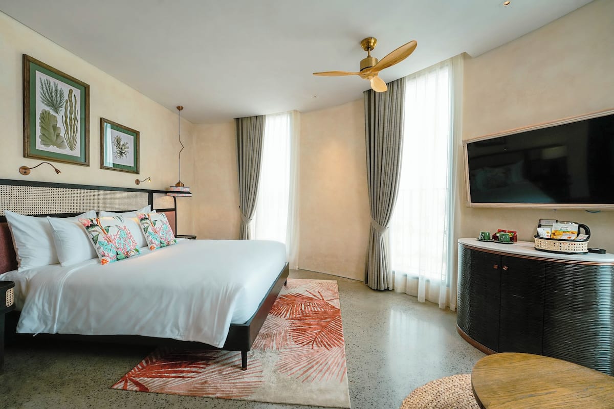 Ein Hotelzimmer mit Bett, Fernseher, Deckenventilator und großem Fenster mit Vorhängen.