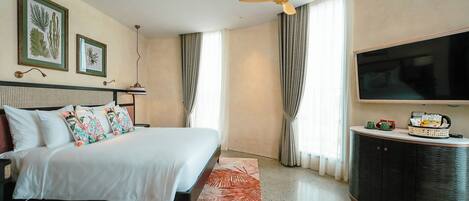 Una habitación de hotel con cama, televisión, ventilador de techo y un gran ventanal con cortinas.