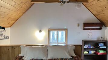 A bedroom with a sloped ceiling, a bed with patterned bedding, a window, and a bookshelf with board games.
